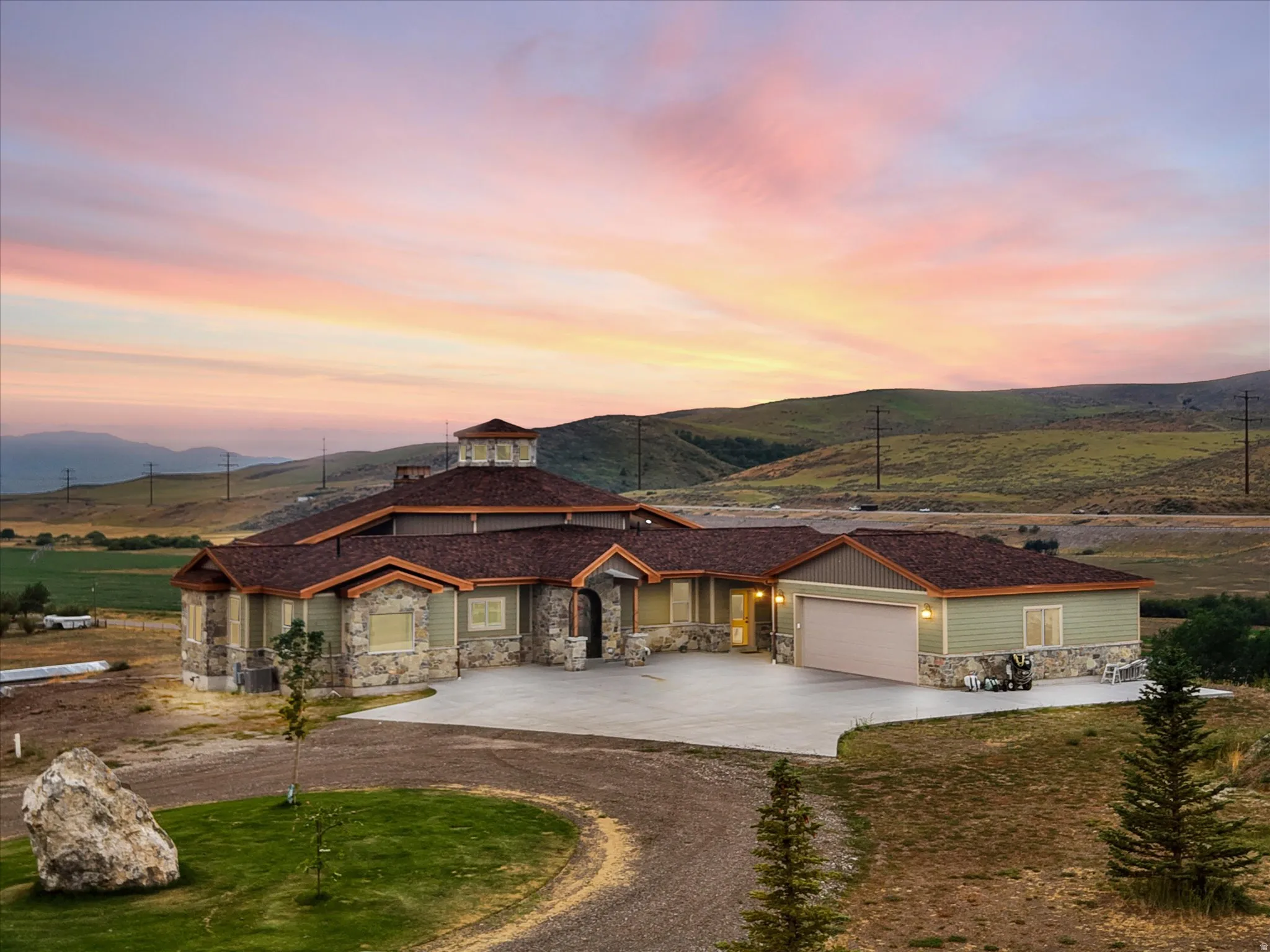 Expansive ranch-style residence featuring stone and siding facade, a prominent cupola, an attached garage, a paved driveway, and a gravel entry drive