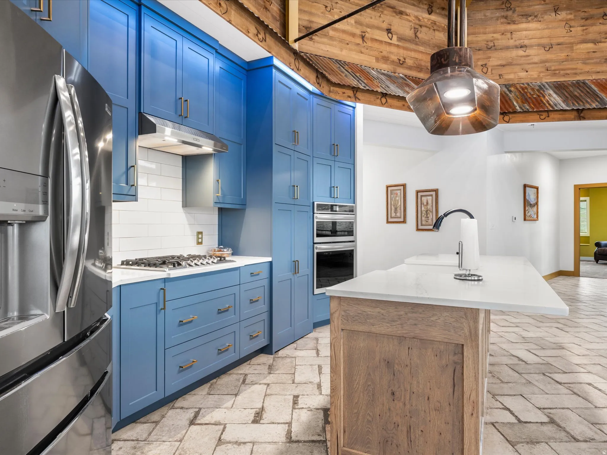 Kitchen featuring blue cabinetry, stainless steel appliances, white subway tile backsplash, and light-toned stone tile flooring