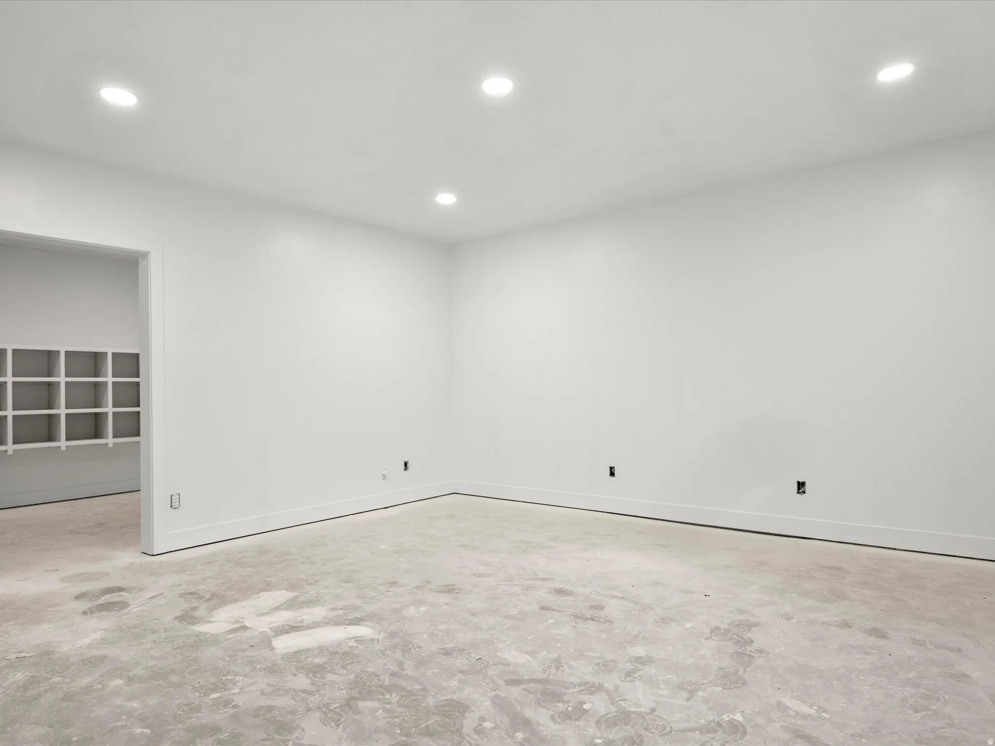Spacious interior room with white walls, recessed ceiling lighting, and a concrete subfloor