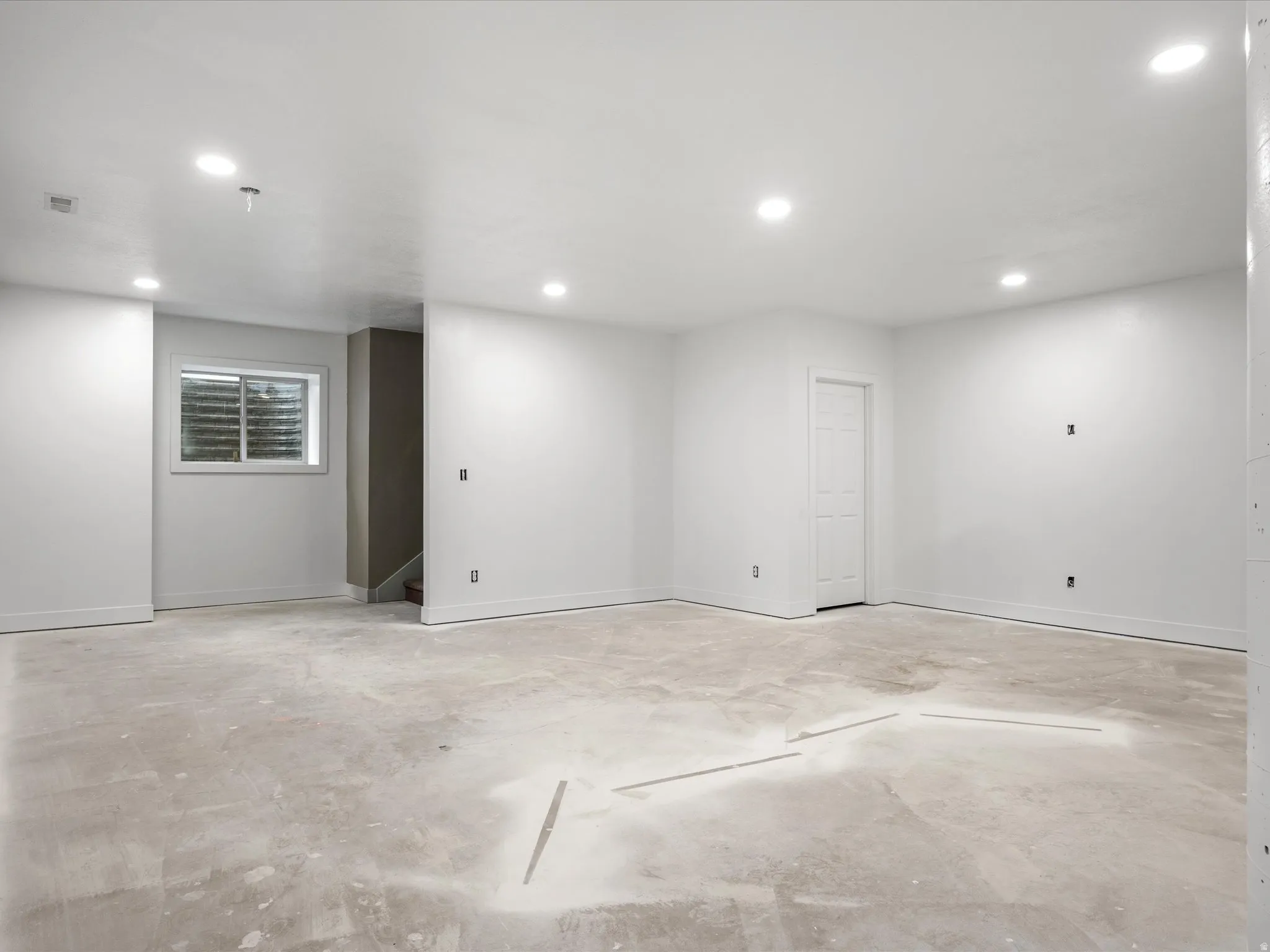 Spacious room featuring a white interior, recessed ceiling lighting, a single white door, and a horizontal window with blinds