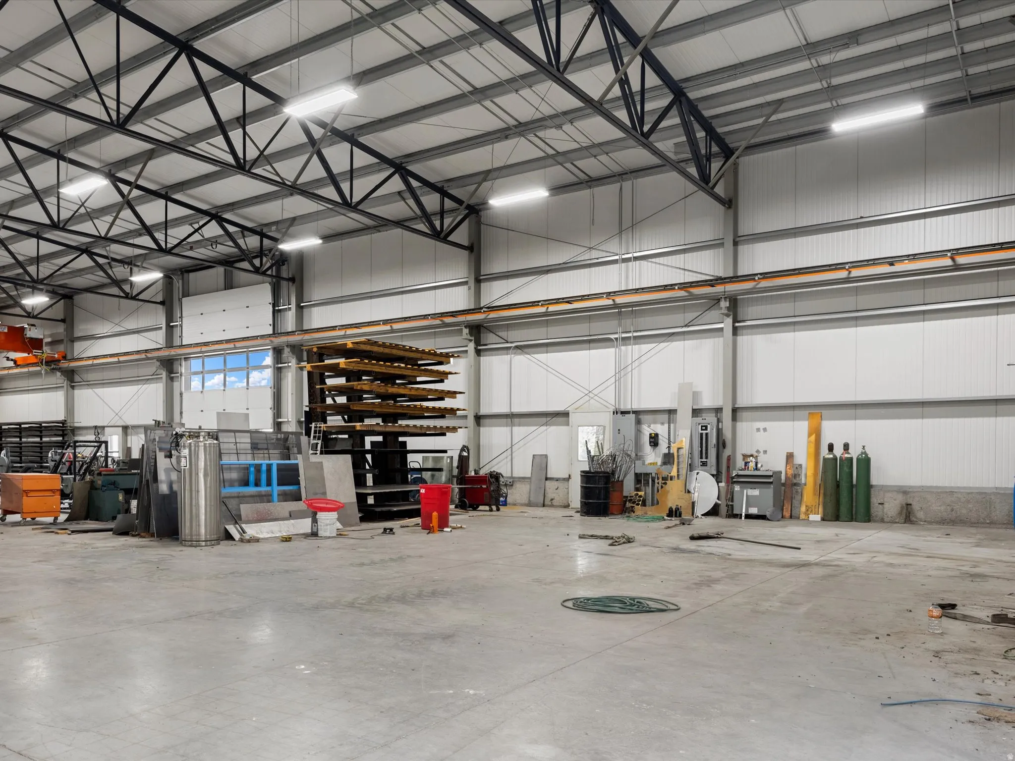 Spacious commercial interior featuring a concrete floor, high ceilings with exposed metal trusses, integrated overhead lighting, and white corrugated metal walls