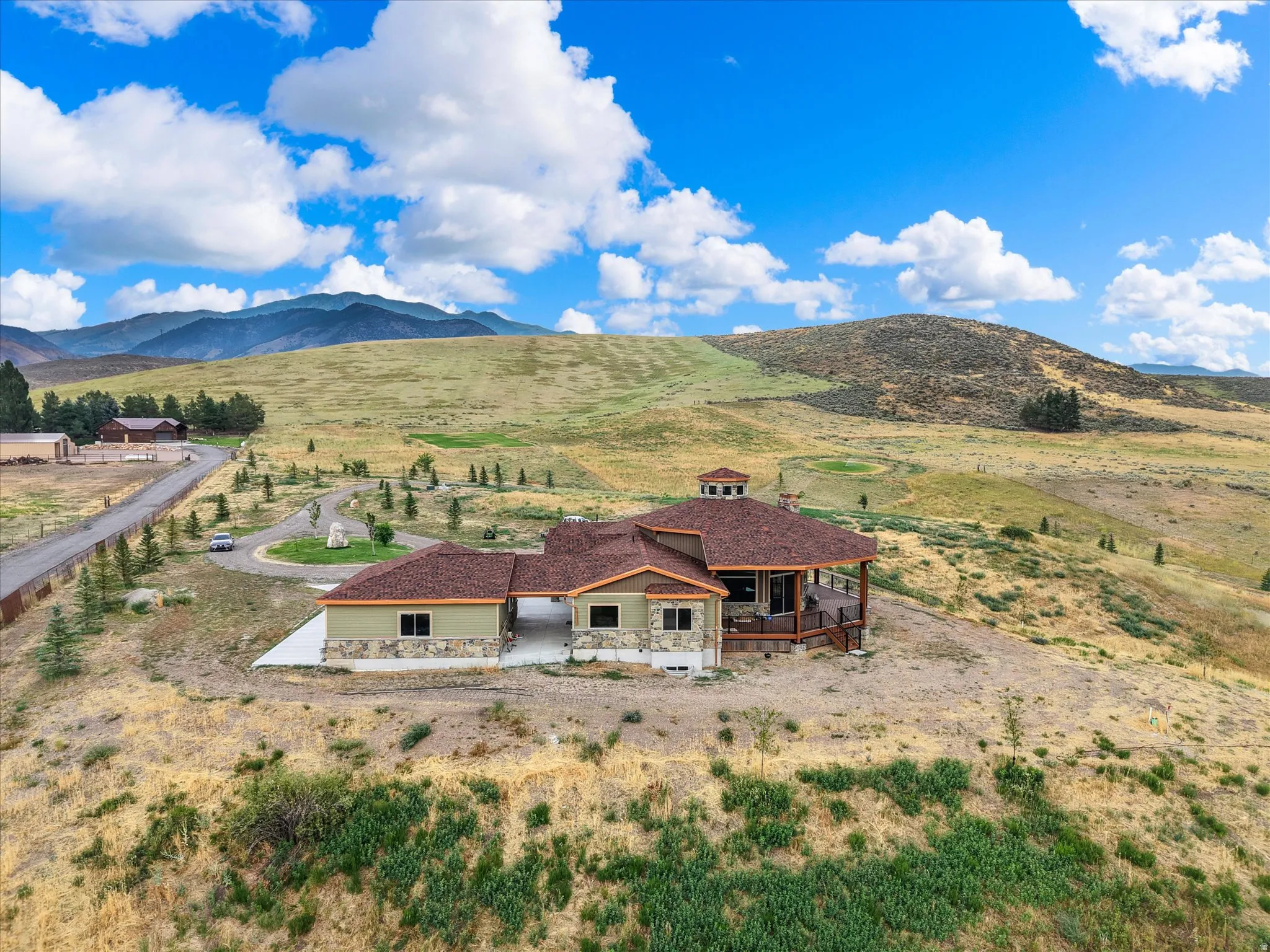 Expansive property featuring a single-story residence with a multi-level roofline, stone veneer accents, and a large covered deck