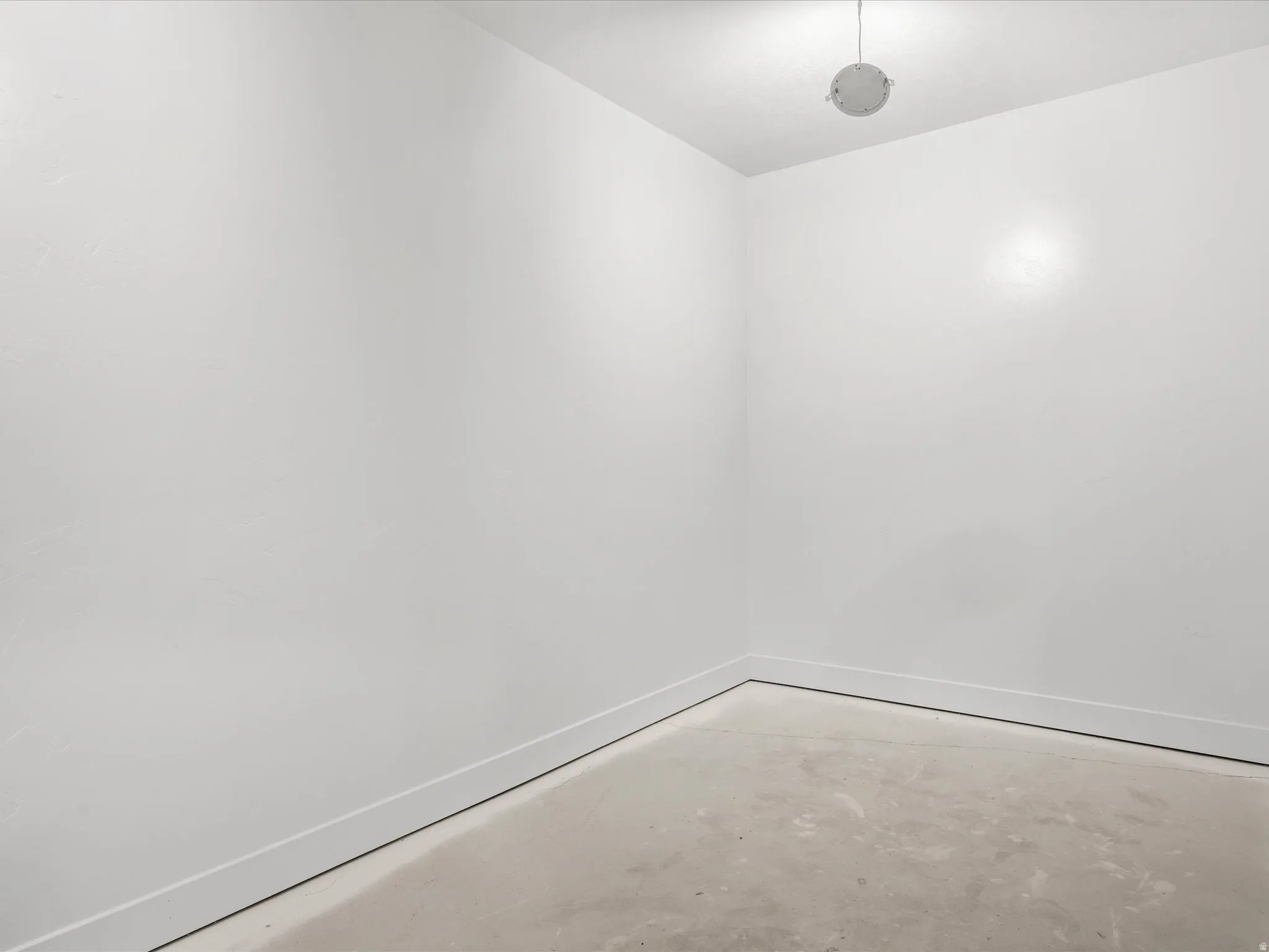 Recessed lighting illuminates a space with white walls and a concrete floor