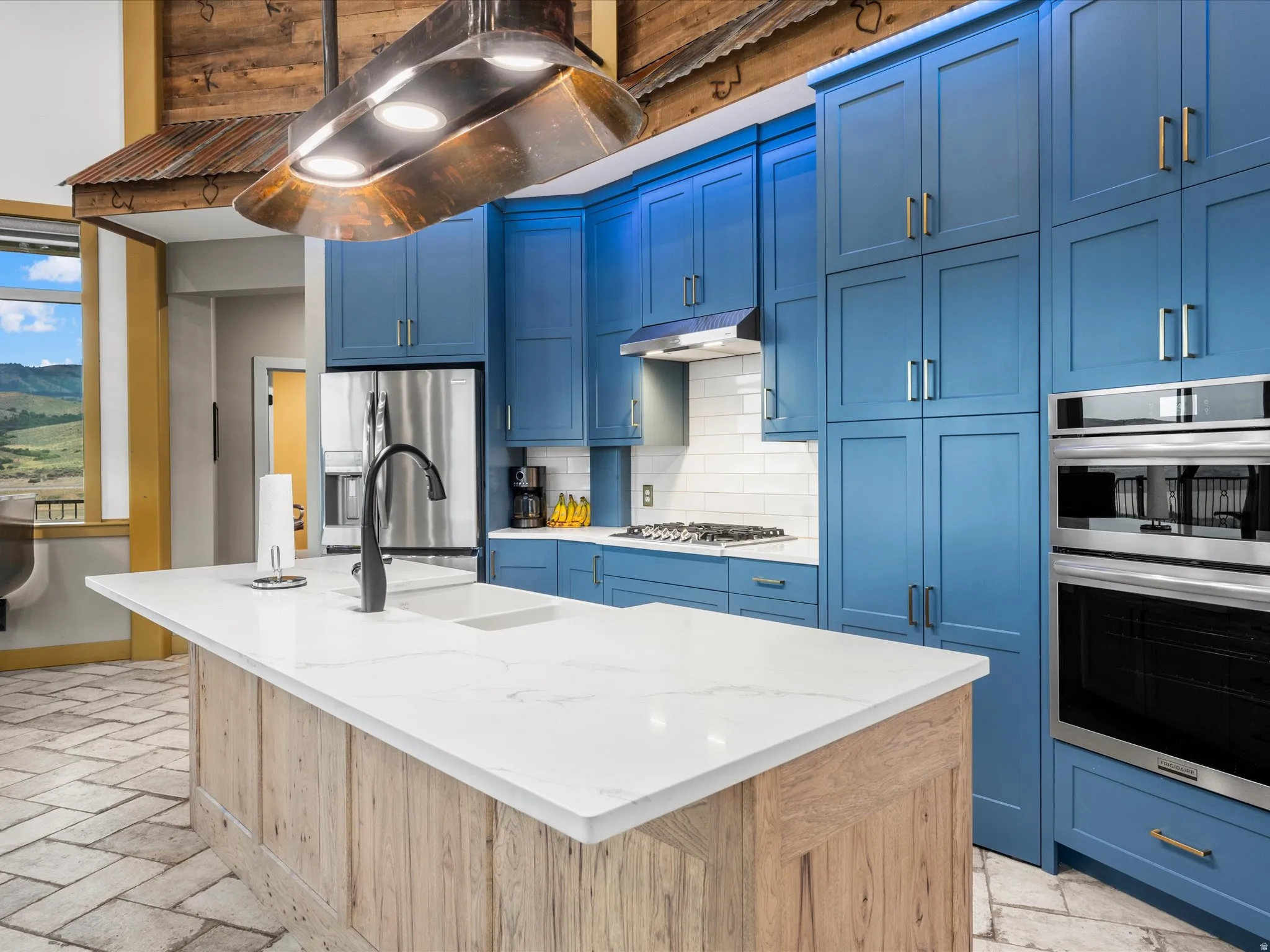 Kitchen featuring blue shaker-style cabinetry, a large center island with wood-finish paneling and a white countertop, subway tile backsplash, stainless steel appliances, and herringbone-patterned tile flooring