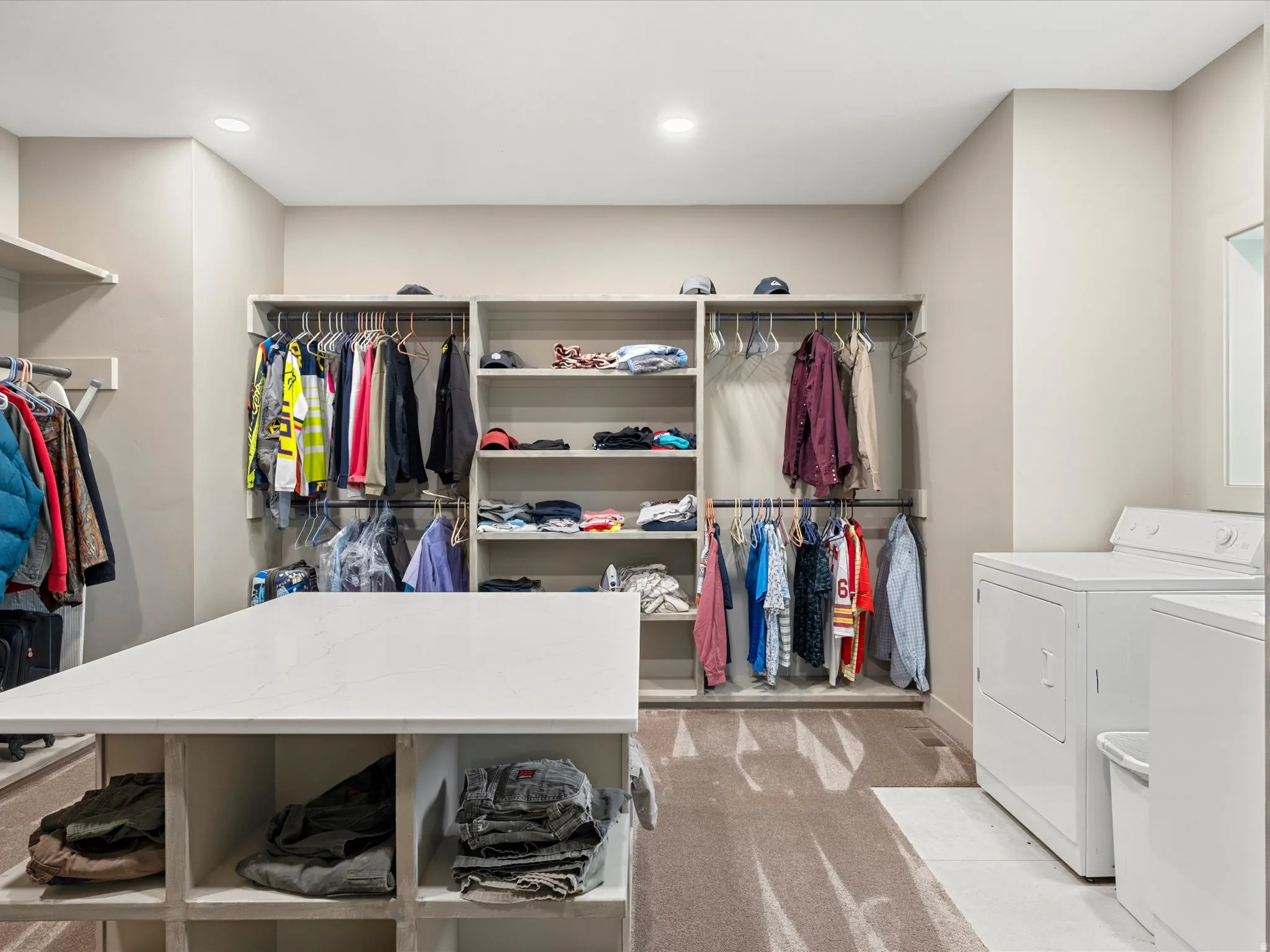 Expansive utility room featuring built-in custom closet organization, a large center island with integrated shelving, and dedicated laundry appliance space