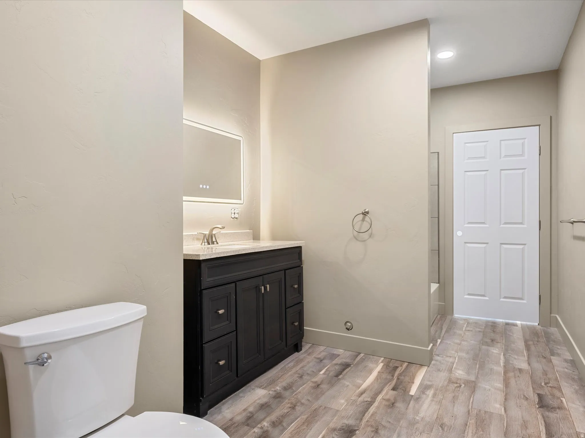 Modern bathroom featuring a dark wood-finish vanity with a light-toned countertop and an illuminated mirror