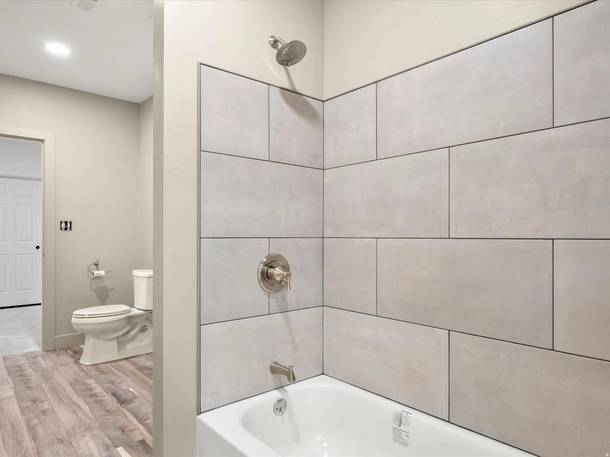 Bathroom featuring a white bathtub, brushed nickel fixtures, light-toned wall tile, wood-finish flooring, and a white toilet