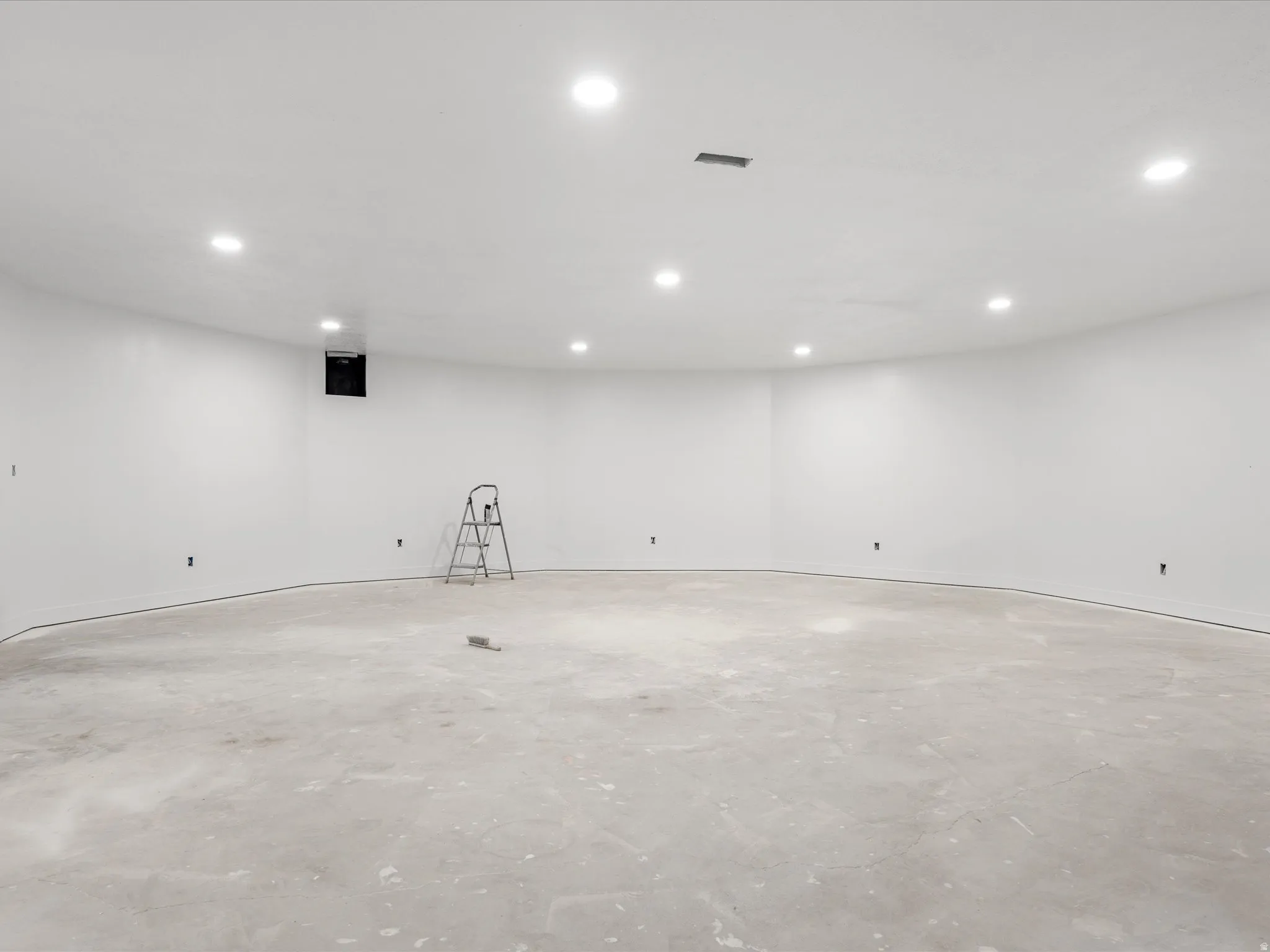 Spacious room with curved walls, recessed lighting, white painted walls, concrete subfloor, and an integrated ventilation system