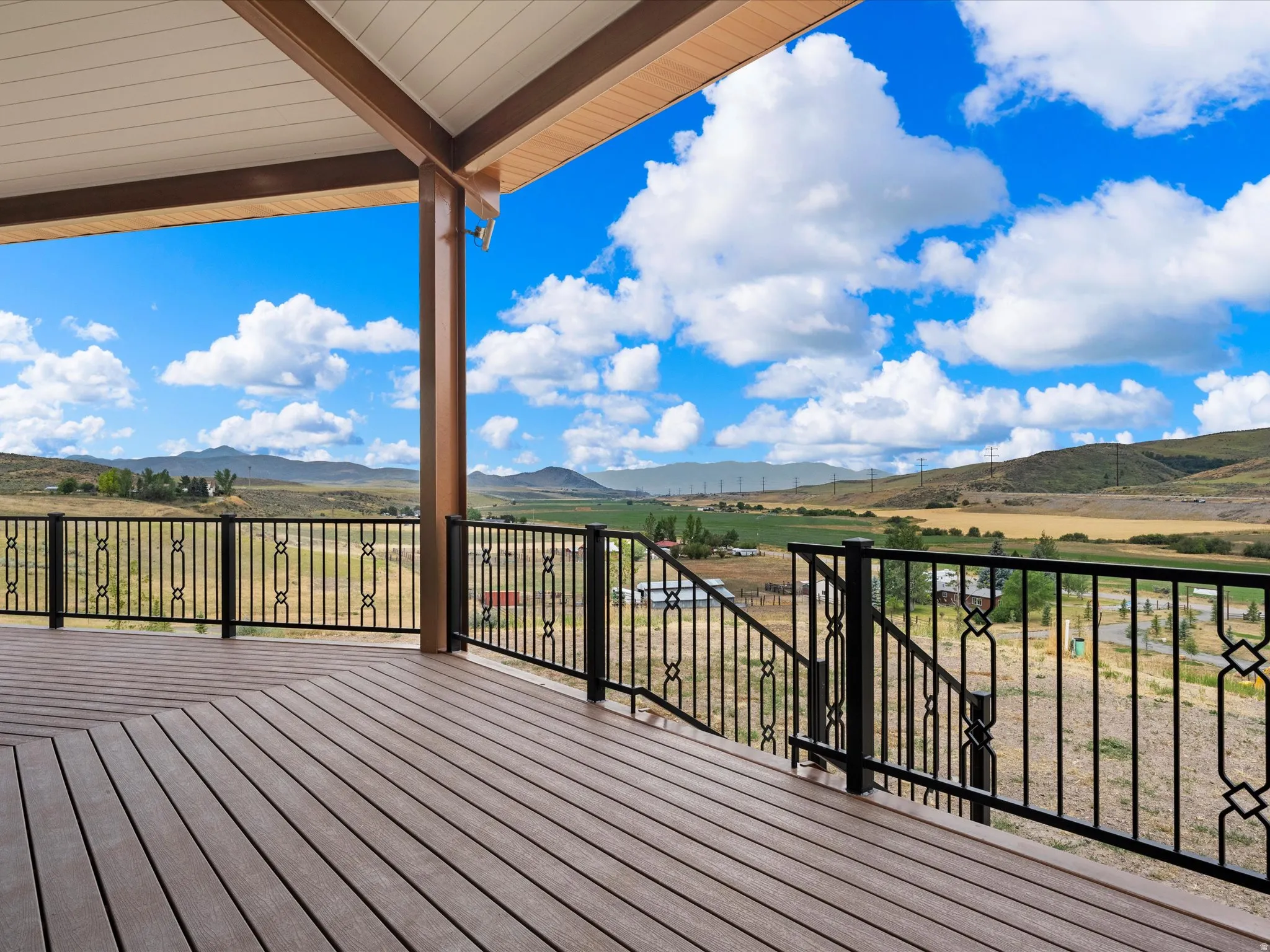Spacious covered deck featuring composite wood-finish flooring and black wrought iron railings with decorative accents