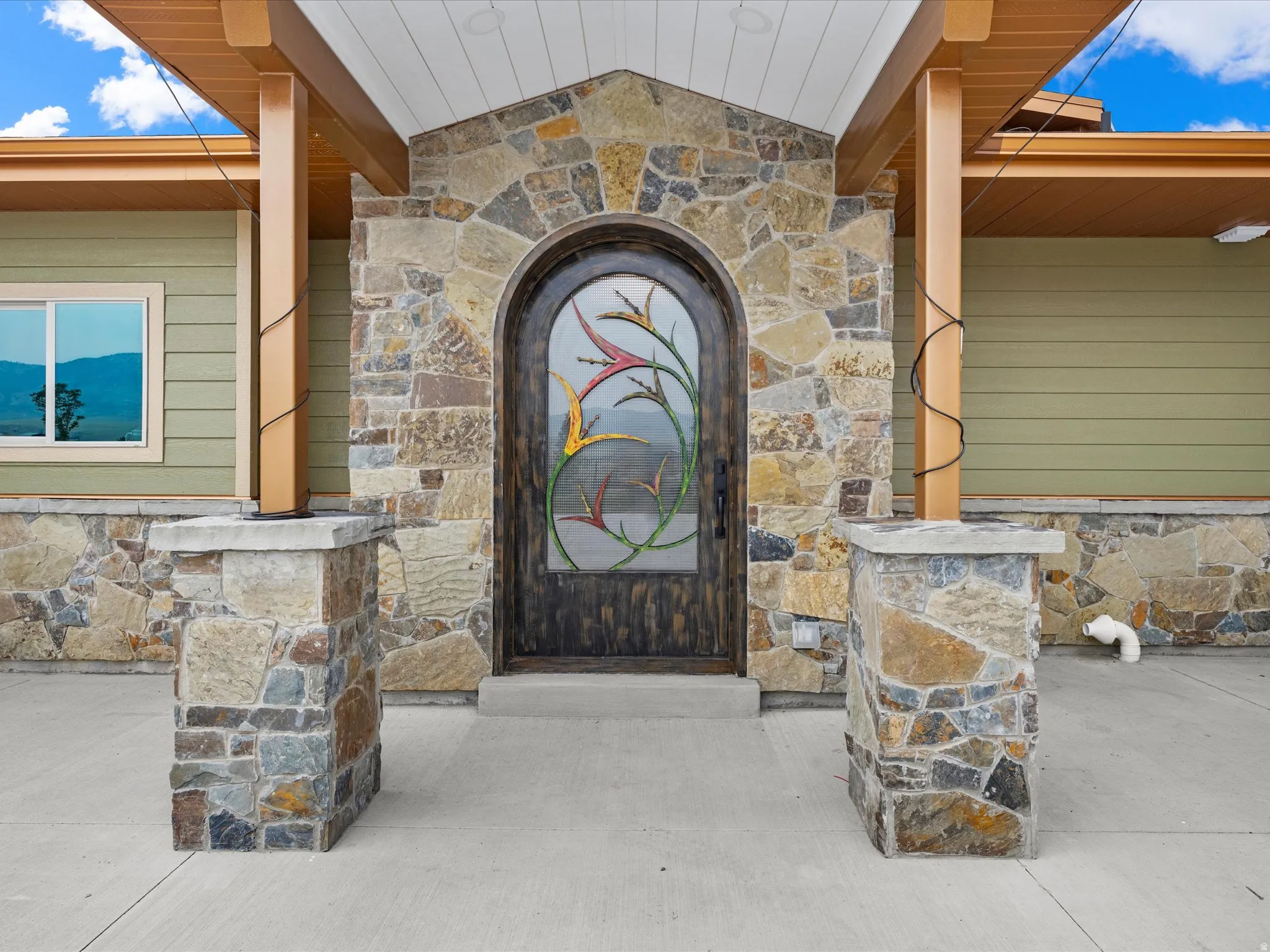Arched entry door with decorative glasswork, framed by natural stone veneer