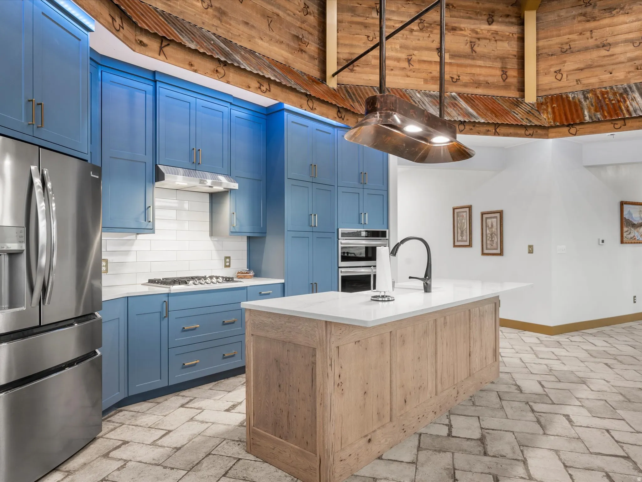 Kitchen featuring blue cabinetry, stainless steel appliances, a white subway tile backsplash, an island with a light wood finish, and herringbone-patterned floor tiles