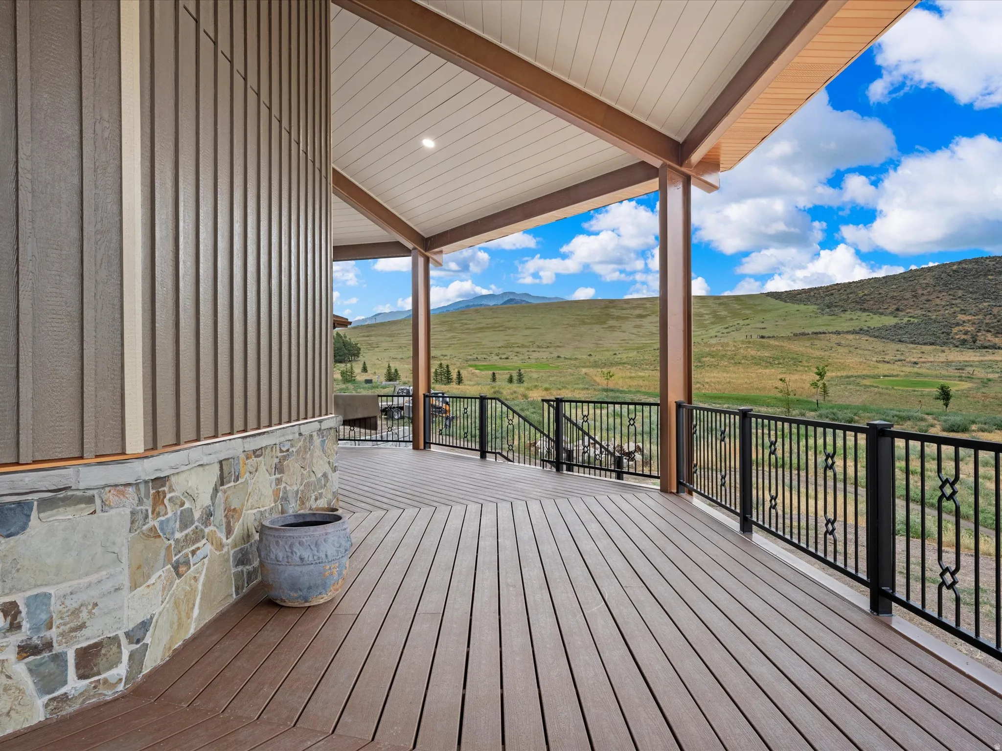 Spacious covered deck featuring composite wood-finish decking, decorative black metal railings, and natural stone veneer accents