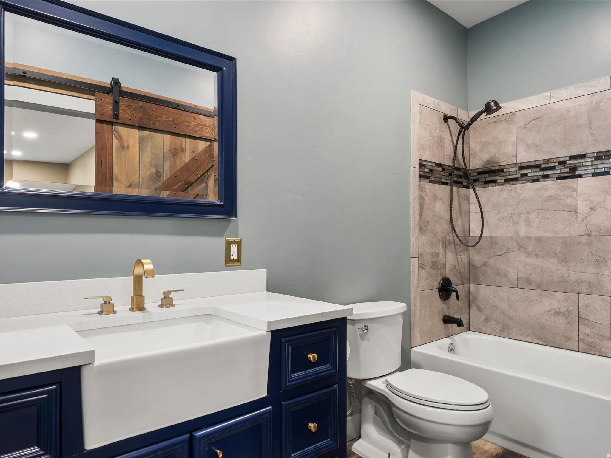 Bathroom featuring a deep blue vanity with gold-tone hardware, a white farmhouse-style sink, and a quartz-finish countertop