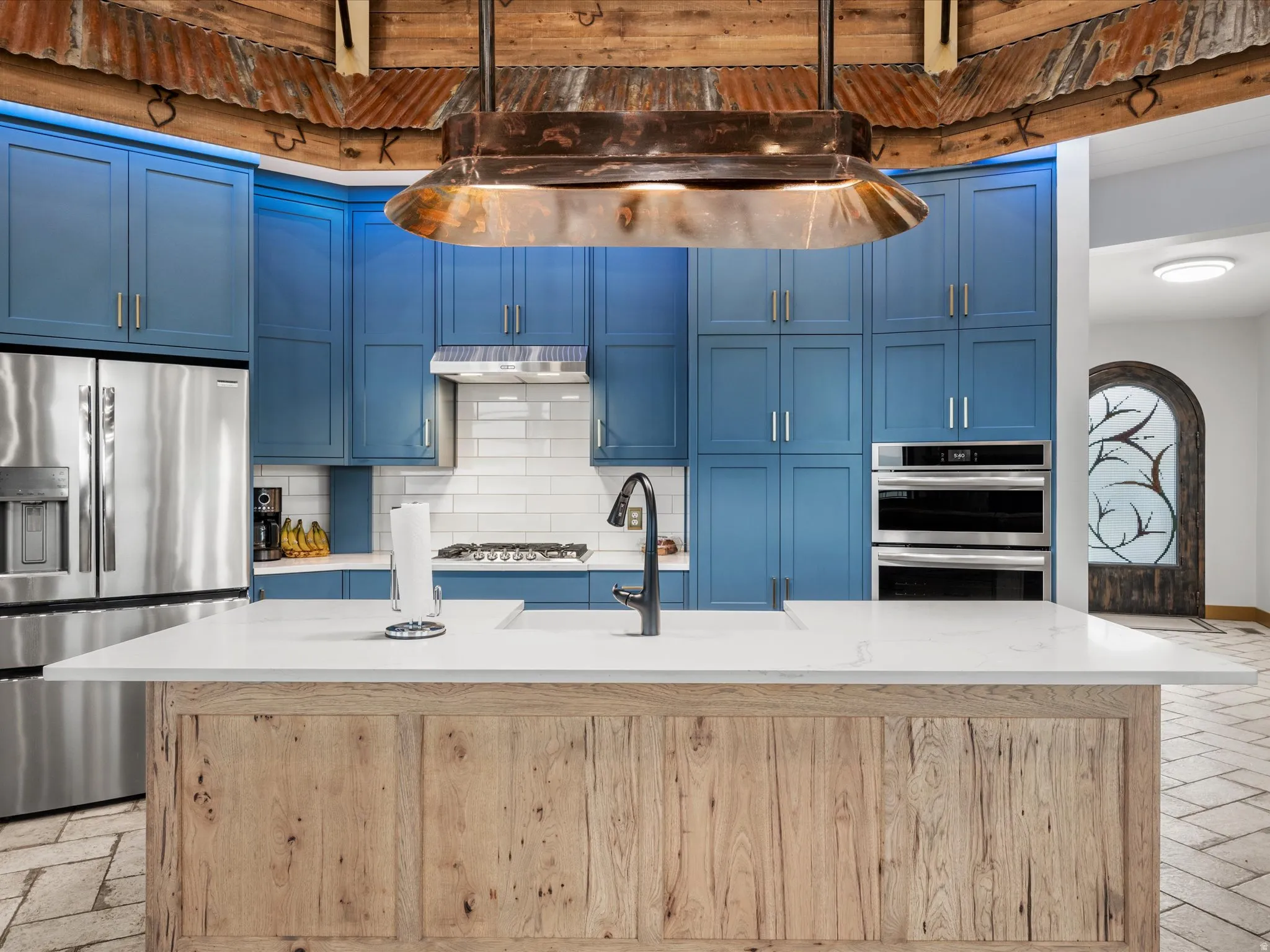 Kitchen featuring a wood-finish island with a white countertop, blue cabinetry, stainless steel appliances, and a tile backsplash
