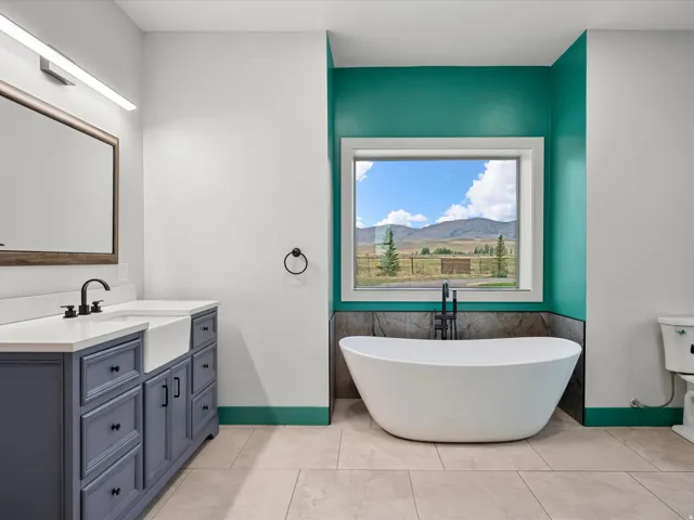 Freestanding soaking tub with floor-mounted faucet, set against a window with mountain scenery