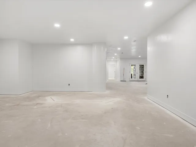 Spacious open-concept room with recessed lighting, white painted walls, and concrete flooring