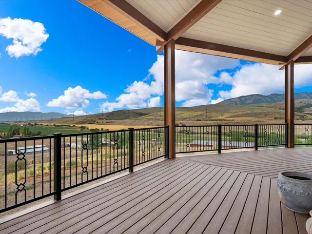 Expansive covered deck featuring wood-finish flooring, black wrought iron railing, exposed wood beams, and recessed lighting