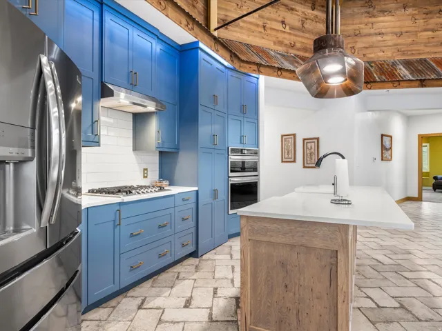 Kitchen featuring blue cabinetry, stainless steel appliances, white subway tile backsplash, and light-toned stone tile flooring
