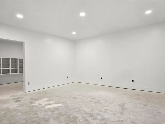 Spacious interior room with white walls, recessed ceiling lighting, and a concrete subfloor