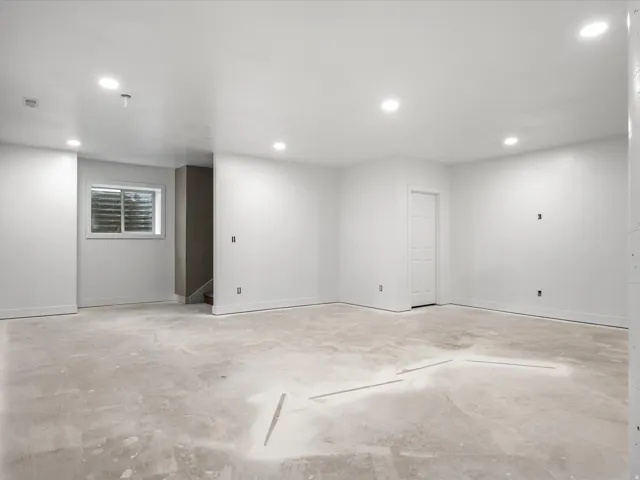 Spacious room featuring a white interior, recessed ceiling lighting, a single white door, and a horizontal window with blinds