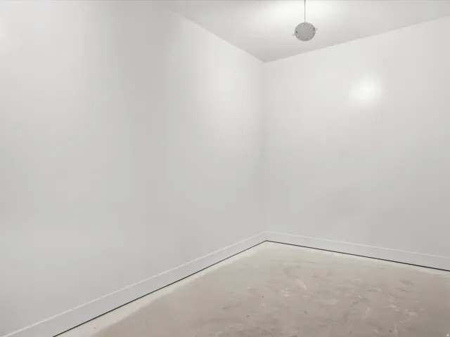 Recessed lighting illuminates a space with white walls and a concrete floor