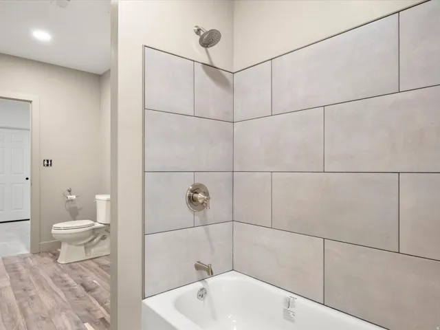 Bathroom featuring a white bathtub, brushed nickel fixtures, light-toned wall tile, wood-finish flooring, and a white toilet