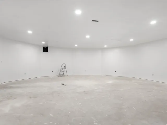 Spacious room with curved walls, recessed lighting, white painted walls, concrete subfloor, and an integrated ventilation system