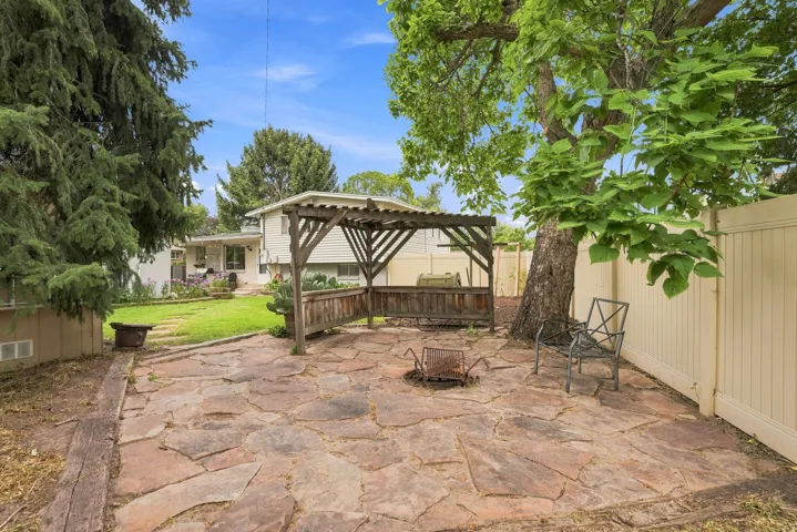 Expansive backyard featuring a natural stone patio, wood pergola, mature trees, and a privacy fence