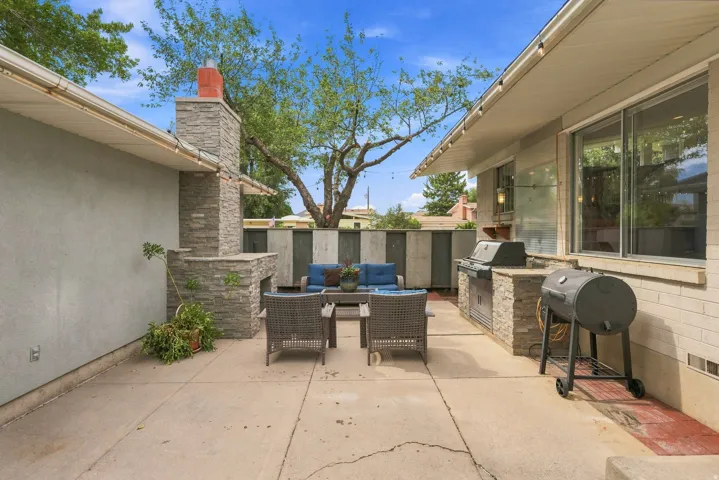 Expansive concrete patio featuring a stone-clad outdoor fireplace, an integrated outdoor kitchen with a built-in grill, and a contrasting light brick exterior wall