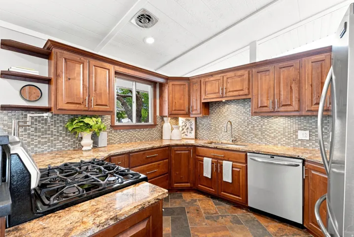Kitchen featuring wood cabinetry, granite countertops, a built-in gas range, stainless steel dishwasher, and a tile backsplash