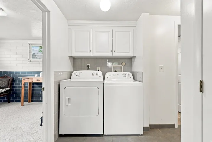 Dedicated laundry area featuring white cabinetry, a light gray tile backsplash, and dark gray floor tiling
