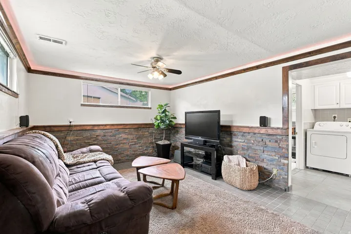 Recreation room featuring stone veneer wainscoting, wood trim accents, and a ceiling fan with integrated lighting