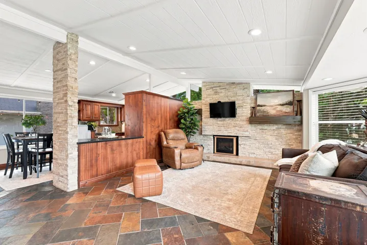Multi-toned slate flooring spans the room, featuring a stone-clad fireplace with a hearth and a wood mantel