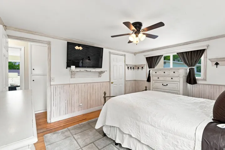 Bedroom featuring wood-finish flooring, built-in shelving, a ceiling fan with integrated lighting, and a window with natural light