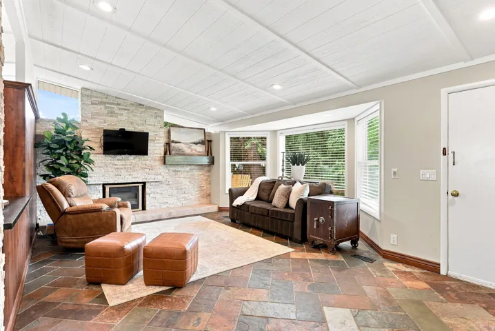 Living area featuring a stone accent wall with a built-in fireplace, a bay window with natural light, wood-finish flooring, and a paneled ceiling with recessed lighting