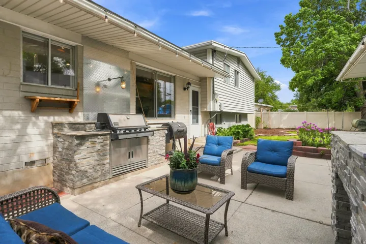 Expansive concrete patio featuring a built-in outdoor kitchen with stone veneer detailing and a stainless steel grill