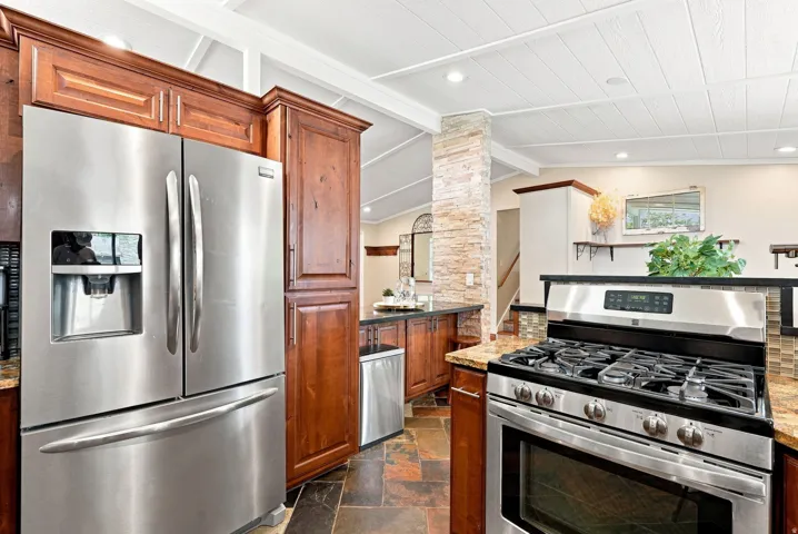 Kitchen featuring stainless steel appliances, wood cabinetry, granite countertops, and slate tile flooring