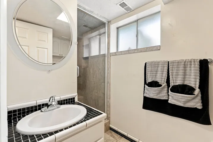 Bathroom featuring a compact vanity with a drop-in sink, black mosaic tile countertop, and a circular mirror
