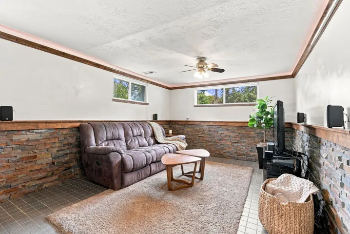Recreation room featuring stone veneer wainscoting, wood trim accents, and a ceiling fan