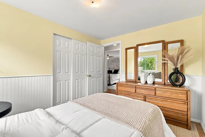Bedroom featuring wainscoting, light yellow wall finish, and wood-finish flooring