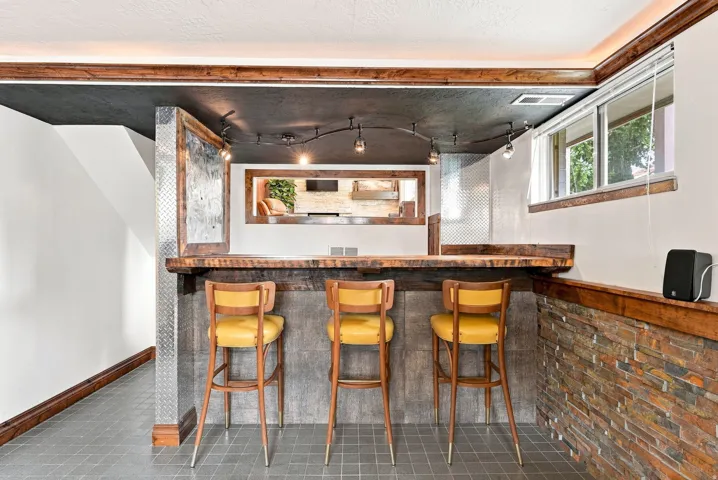 Custom built-in bar featuring a wood-finish countertop, stone accent wall, and track lighting
