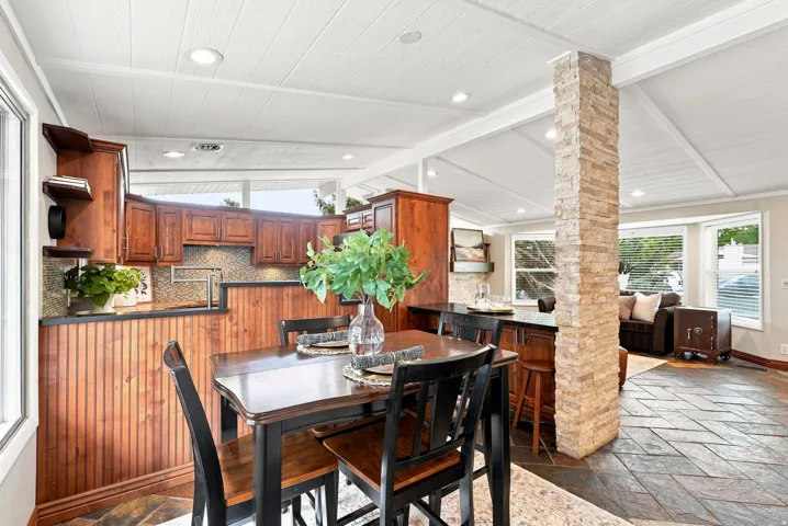 Open-concept interior featuring a breakfast bar with wood cabinetry, a stacked stone column, and a dining area with a dark wood table