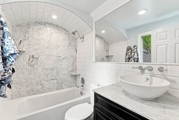 Bathroom featuring a white subway tile surround, vessel sink, and an arched alcove with stone-finish tiles