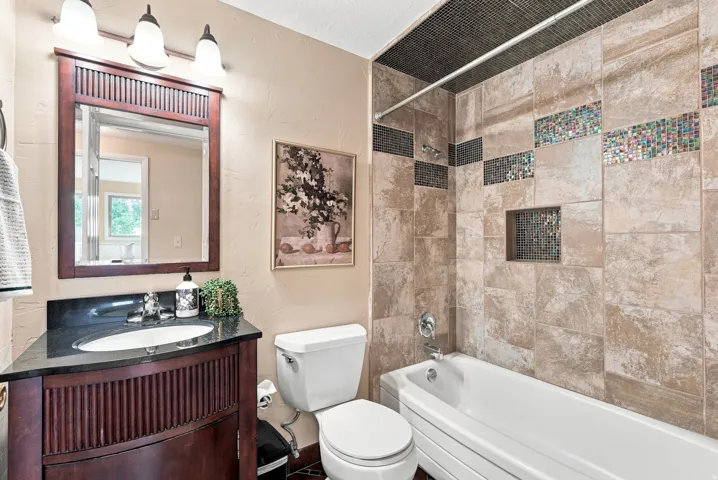 Full bathroom featuring a dark wood-finish vanity with a dark countertop and undermount sink, a toilet, and a bathtub with a tiled surround