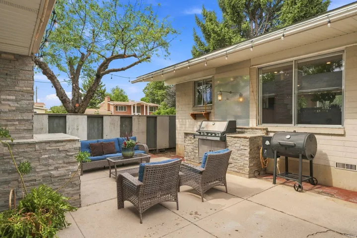 Expansive concrete patio featuring a built-in outdoor kitchen with a gas grill, stone veneer accents, and string lighting