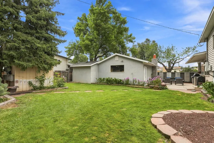 Expansive lawn with a stone-edged planting bed, a separate auxiliary structure, and a hardscaped patio area