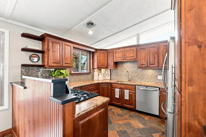 Kitchen featuring rich wood cabinetry, granite-finish countertops, stainless steel appliances, a tiled backsplash, and slate-style flooring