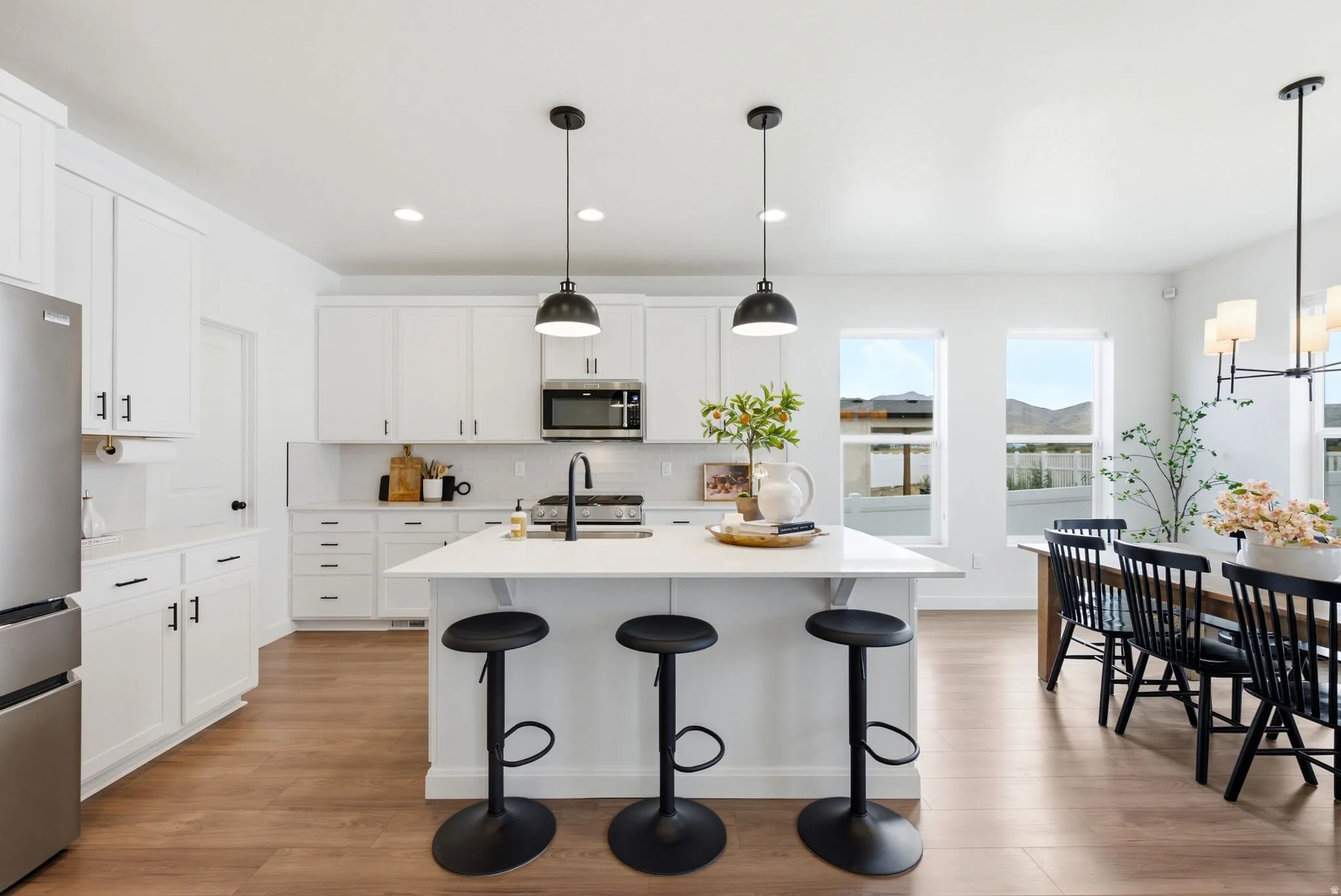 Contemporary kitchen featuring white cabinetry, stainless steel appliances, a center island with pendant lighting, a black sink faucet, and wood-finish flooring