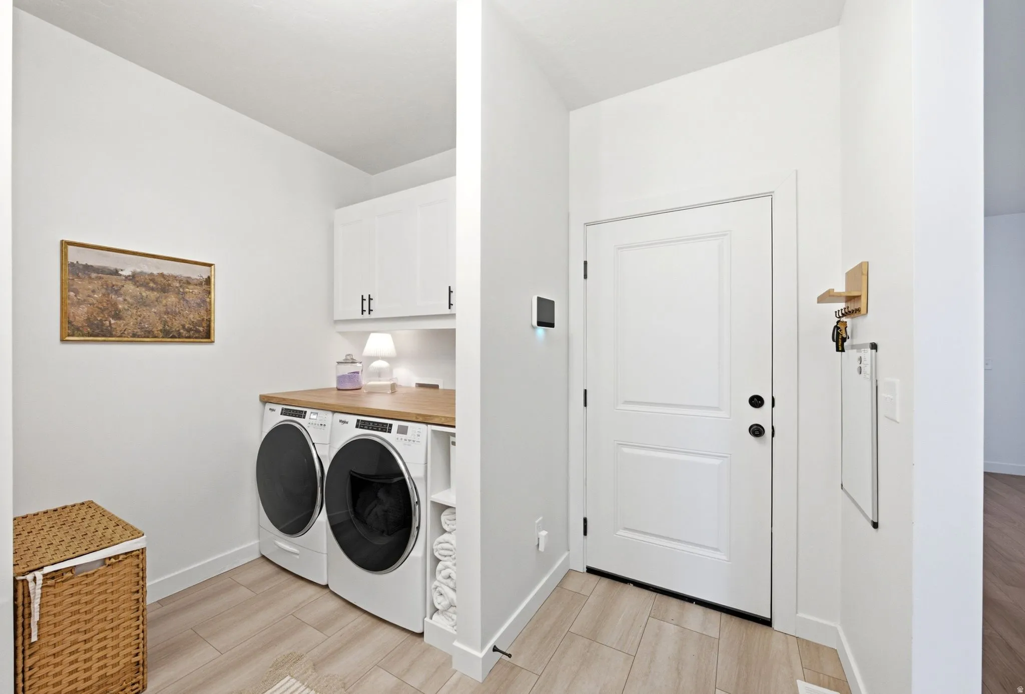 Laundry area featuring a wood-finish countertop, white cabinetry with dark hardware, and light wood-finish flooring