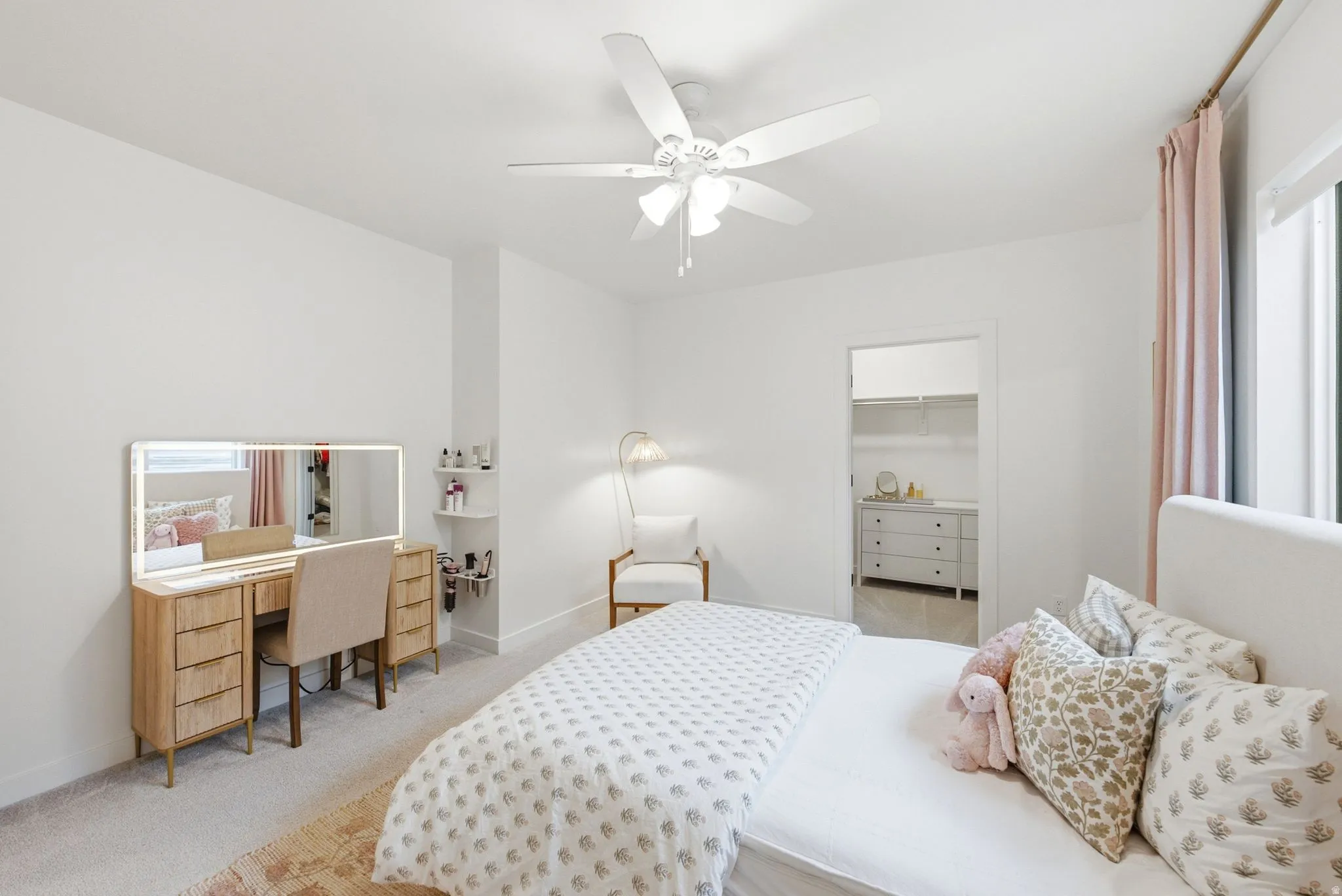 Spacious room featuring light-toned walls, ceiling fan, carpet flooring, a walk-in closet, and a window with roller shades